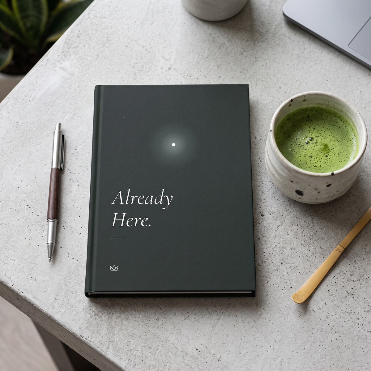 Forest-green Already Here journal on a stone table next to a cup of matcha and a pen