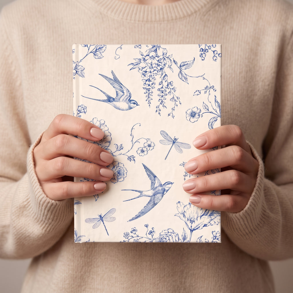 Hands holding the blue and cream Toile de Jouy journal against a beige sweater
