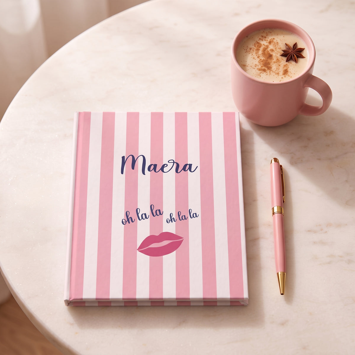 Pink striped Oh La La journal with custom name on a table next to a cup of coffee and a pen