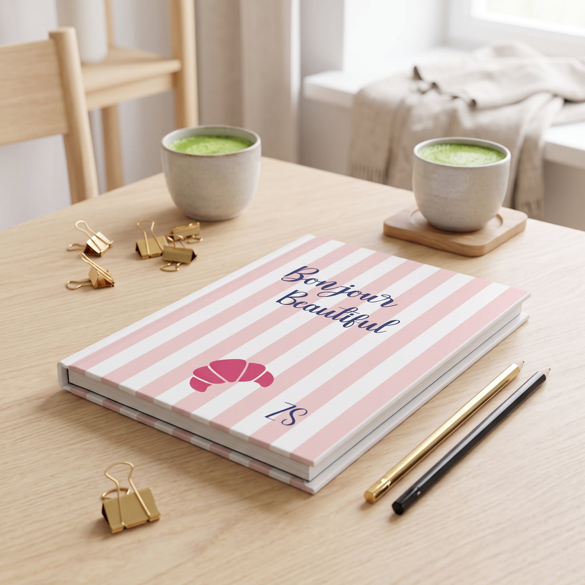 Pink striped Bonjour Beautiful journal on a wooden table with cups of coffee and pencils