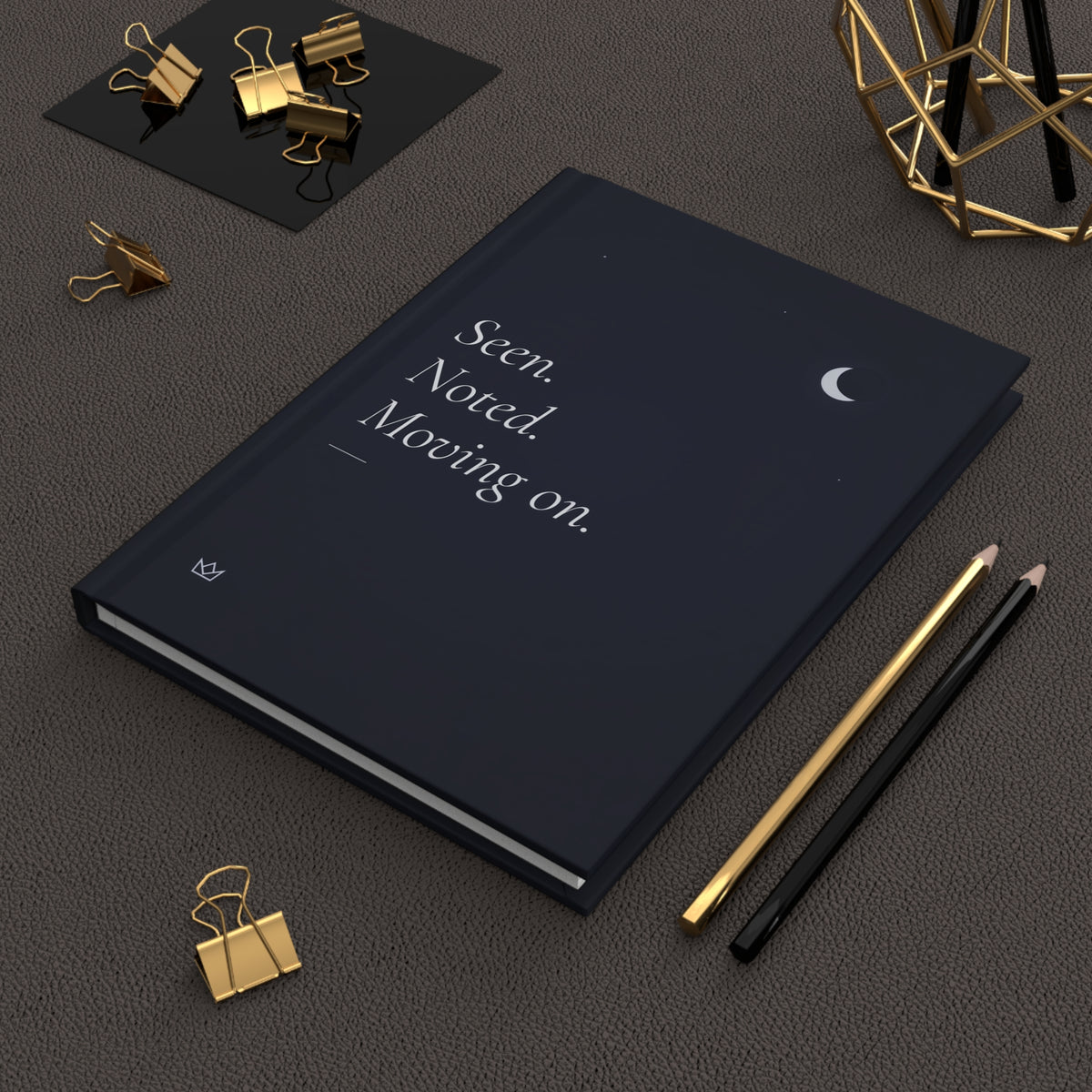 Night-blue moon journal in a dark flat lay with gold pens and paper clips