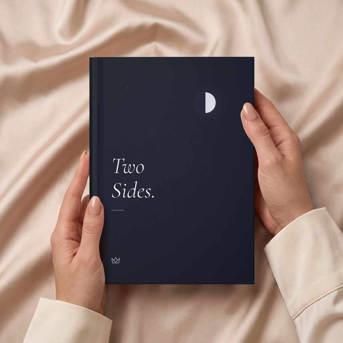 Hands holding the night-blue Two Sides journal over soft beige fabric