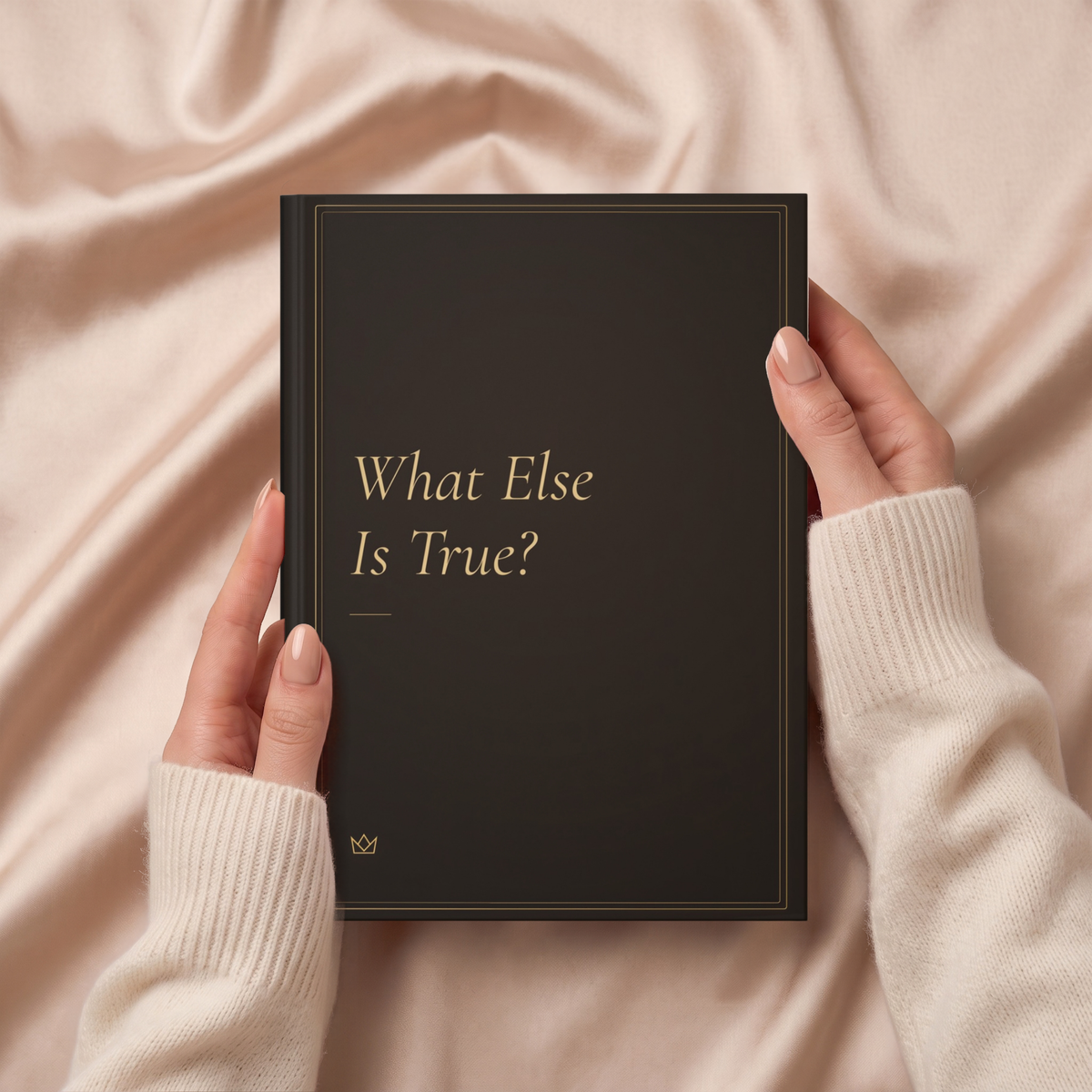 Hands holding the deep brown What Else Is True? journal over soft beige fabric